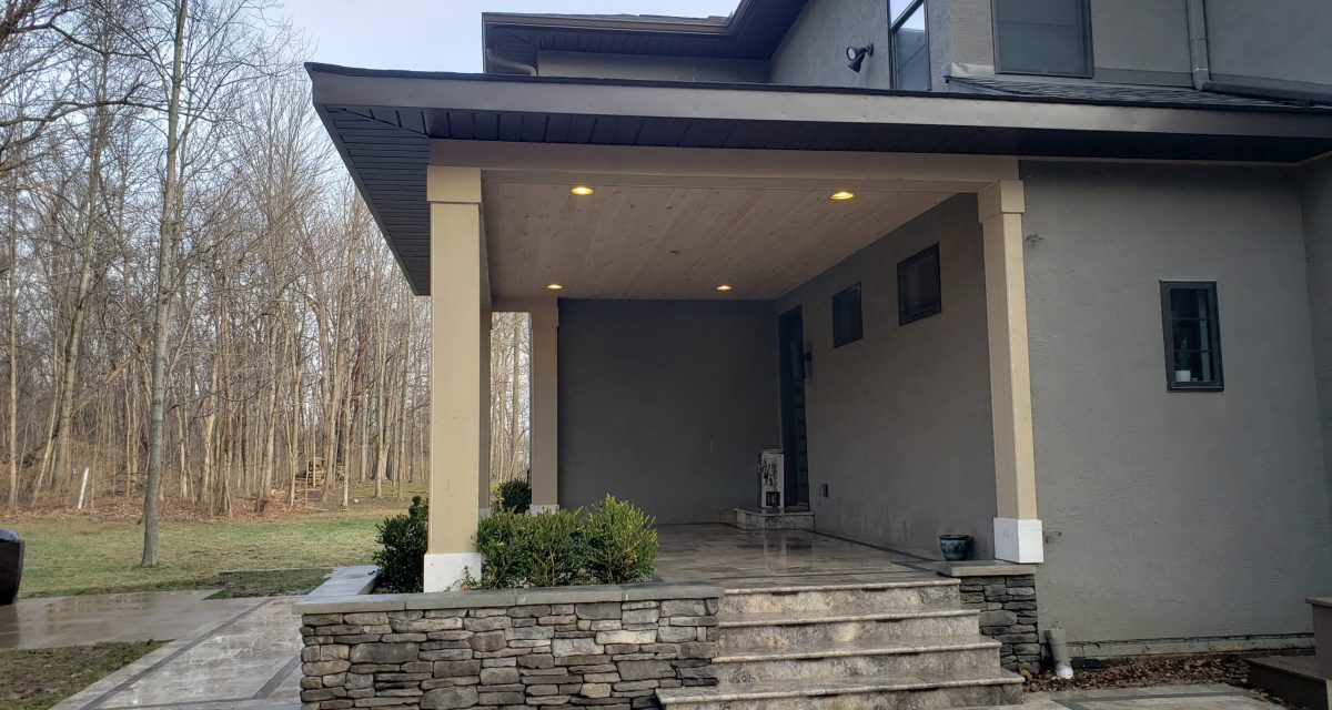 1894 Modern home entrance with stone steps, covered porch, and wooden ceiling, surrounded by trees, reflecting ALC Outdoor Creations' commitment to innovative outdoor design.